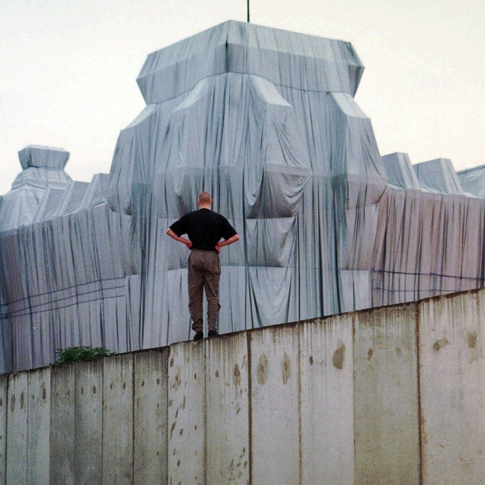 A man stands at the top of remains of the Berlin Wall and looks at the wrapped Reichstag building, a project titled Wrapped Reichstag by American artist Christo and his wife Jeanne-Claude