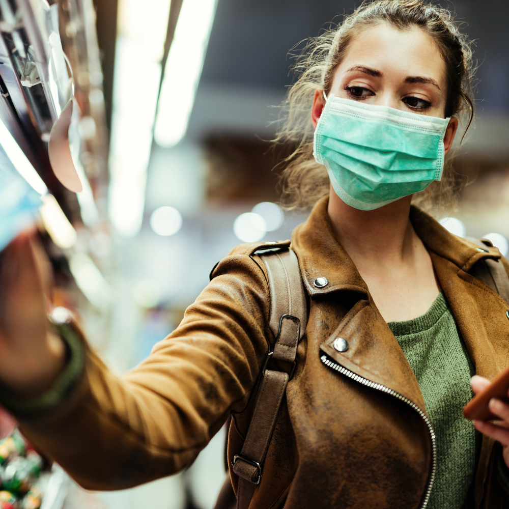 Woman wearing protective mask while using cell phone and buying food in grocery store